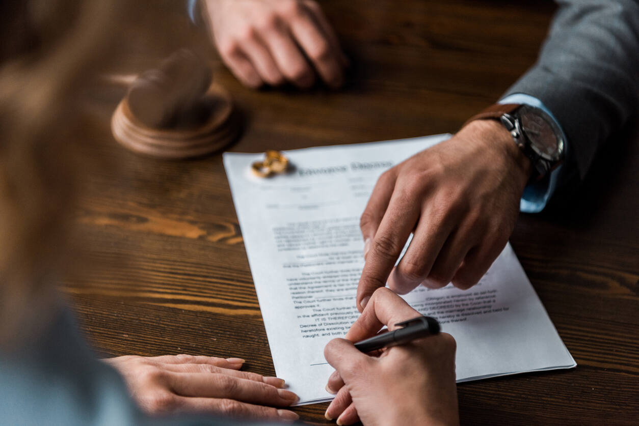 A man and woman's hands on a legal document with a pen and wedding rings nearby, symbolizing the process of hiring a St. Lucie County divorce lawyer.