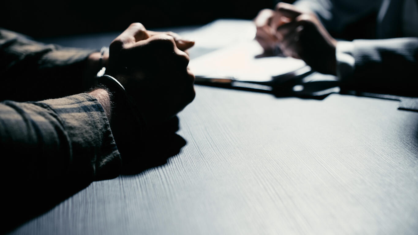 Close-up of a person in handcuffs sitting at a table during a meeting with a legal professional, symbolizing criminal court proceedings.