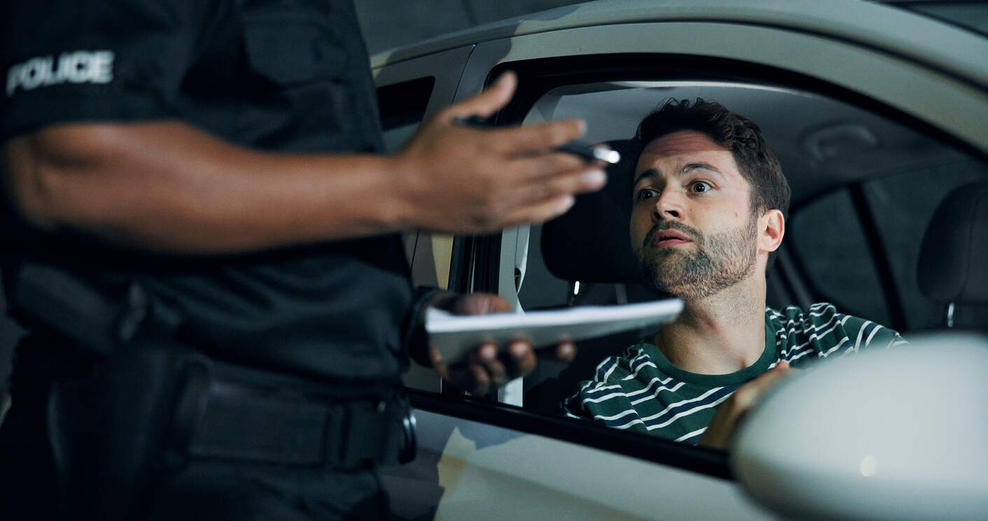 A man in a car looking at a police officer holding a citation during a traffic stop, symbolizing a DUI offense and potential legal consequences.