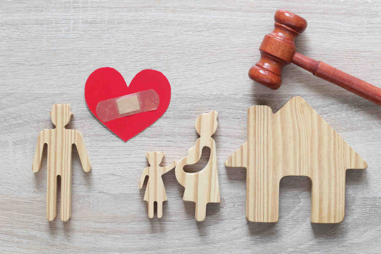 Wooden figures of a family (man, child, pregnant woman), a house, a heart with a bandage, and a gavel, symbolizing child support and family law.