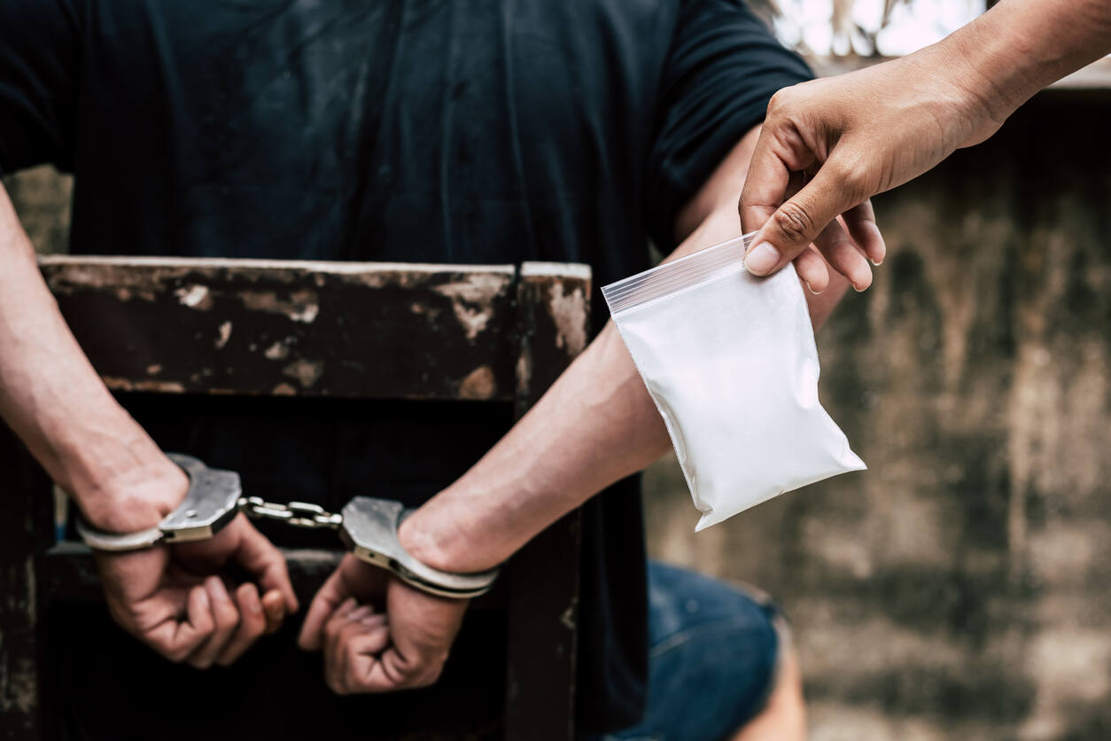 Image showing a person in handcuffs with a bag of drugs, illustrating the difference between drug possession and drug trafficking